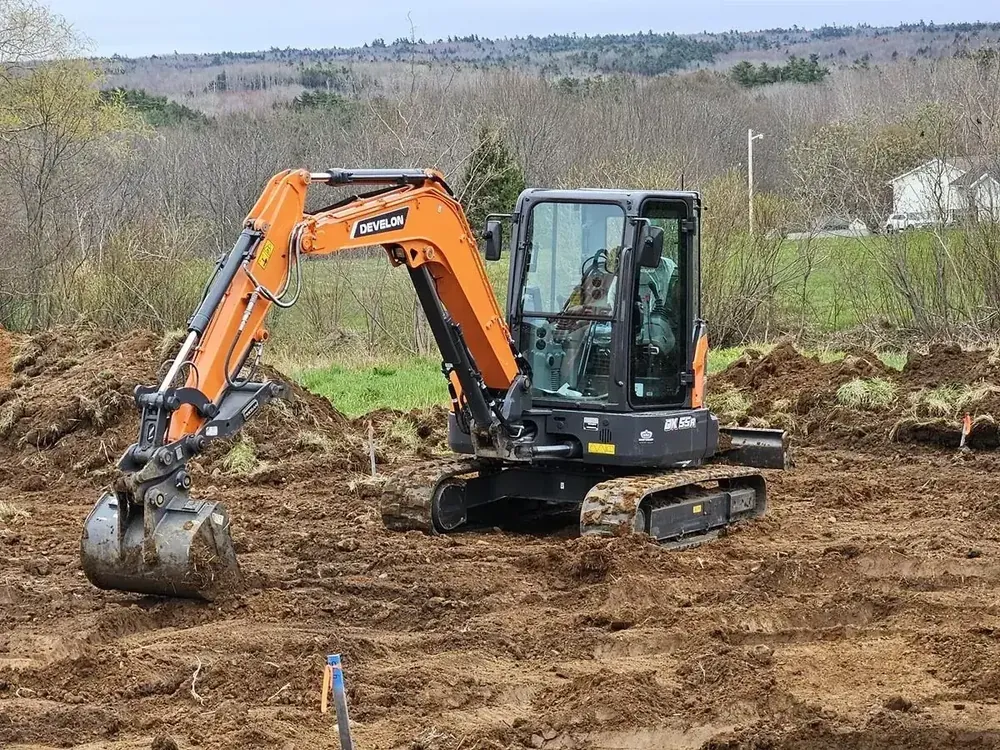 A Wildawbren 5.5-ton orange mini excavator parked mid-dig on a freshly-worked Nova Scotia building site, surrounded by mounded earth