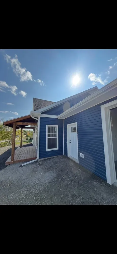A finished Wildawbren navy blue home from the side, white trim, covered porch, and a side door overlooking the Annapolis Valley
