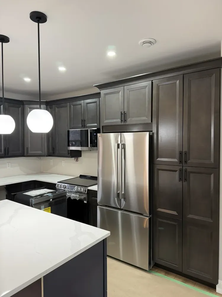 A Wildawbren kitchen with espresso raised-panel cabinets, stainless French-door fridge, glass globe pendants, and a quartz waterfall island